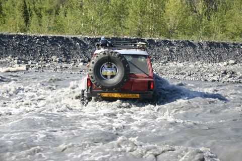 2003 Jeep TJ - A red 2003 Jeep TJ navigates a rocky riverbed, kicking up water as it drives through the current.