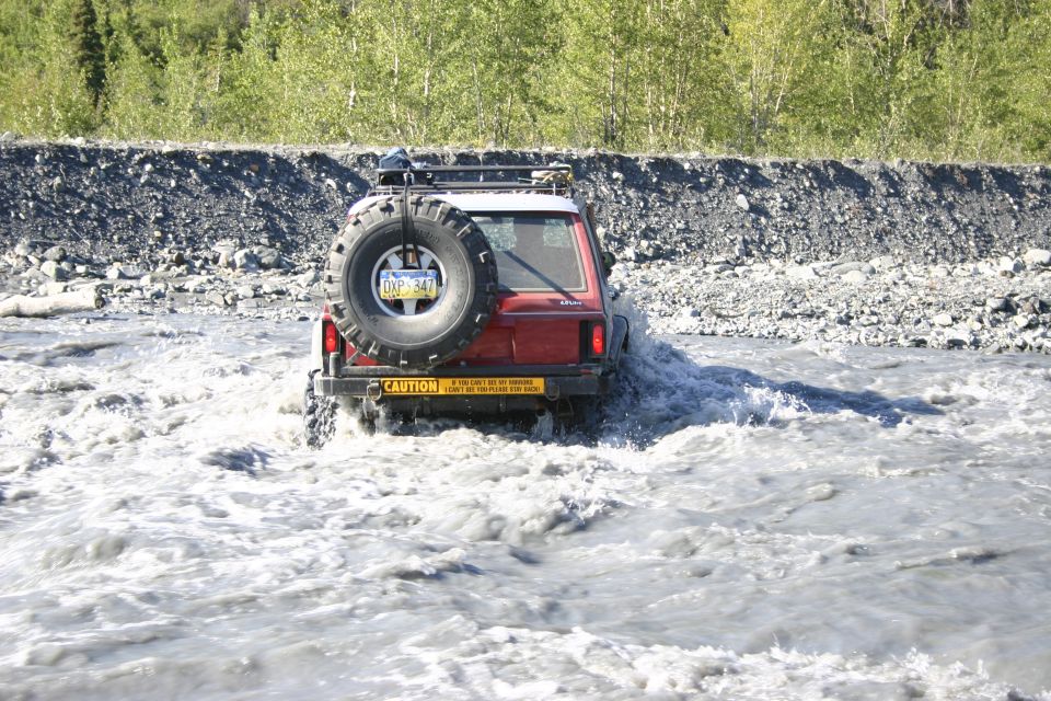 Red 2003 Jeep TJ driving through a rocky riverbed with trees in background