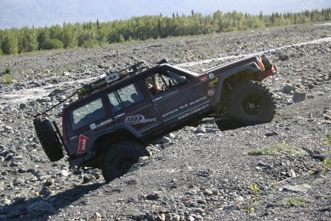 2003 Jeep TJ - A dark red Jeep Cherokee XJ navigates a challenging rocky incline, its off-road capabilities.