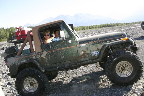 2003 Jeep TJ - Two people in a green Jeep Wrangler TJ navigate a rough, rocky terrain under a clear sky.