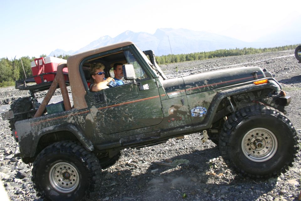 Green Jeep Wrangler TJ with two people inside, driving on a rocky, off-road trail with mountains in the background