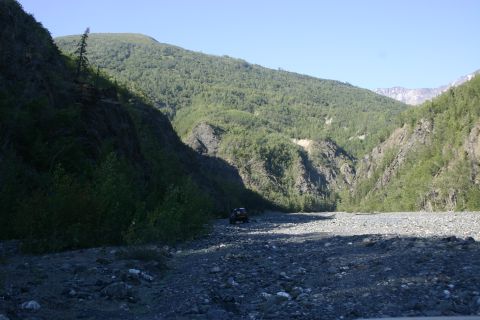 2003 Jeep TJ - A Jeep Wrangler navigates a , rocky terrain surrounded by lush green mountains under a clear blue sky.