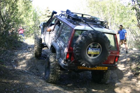 2003 Jeep TJ - A heavily modified Jeep Cherokee XJ navigates a challenging off-road trail with a spare tire mounted on the rear.