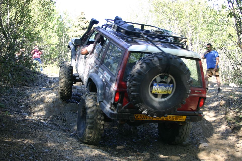 modified Jeep Cherokee XJ climbing a dirt trail, spare tire mounted on back