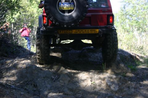 2003 Jeep TJ - A red Jeep TJ navigates a challenging rocky terrain on a wooded trail.