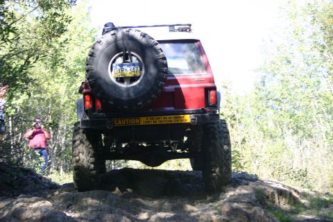 2003 Jeep TJ - A red 2003 Jeep TJ navigates a challenging off-road trail with a spare tire mounted on the rear.