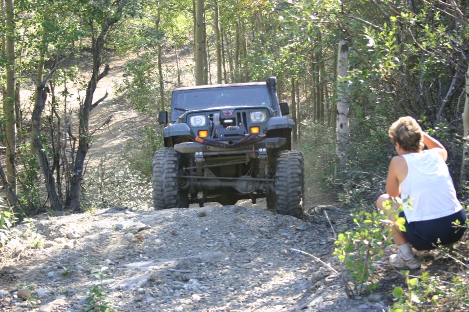 Dark grey Jeep Wrangler with large tires and snorkel, front view, on a dirt trail