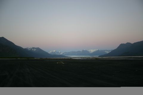 2003 Jeep TJ - A vast, dark landscape unfolds with tire tracks leading towards a tranquil body of water and distant, snow-capped mountains at twilight.