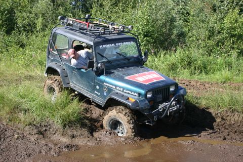 2003 Jeep TJ - A Jeep Wrangler navigates a muddy off-road trail, its front-left wheel deep in the mire.