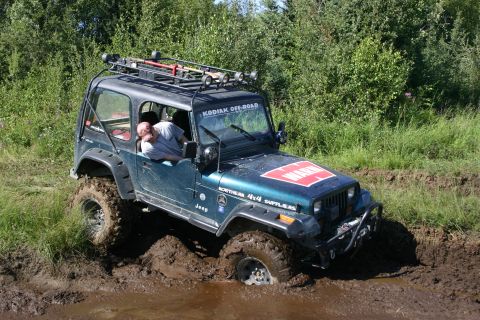 2003 Jeep TJ - A dark green Jeep Wrangler navigates a muddy off-road course, its tires deep in the mire. Text on the windshield reads "KODIAK OFF-ROAD".