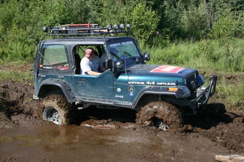 2003 Jeep TJ - Jeep Wrangler deep in mud, with a roof rack and off-road accessories visible.