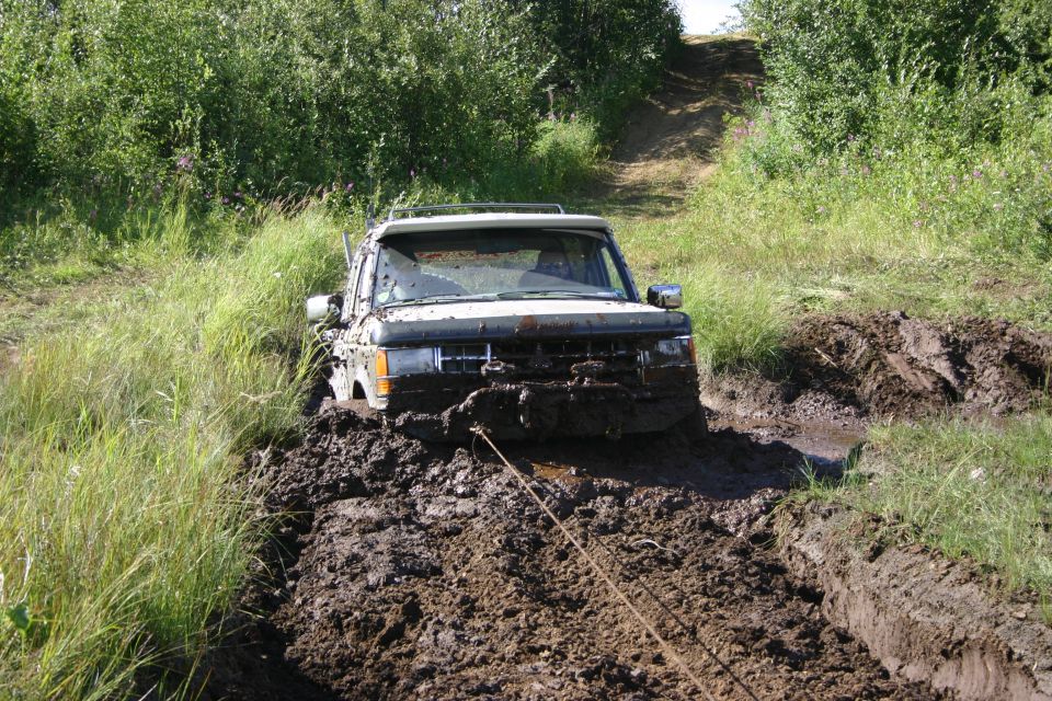 White SUV stuck in deep mud, being pulled by a rope