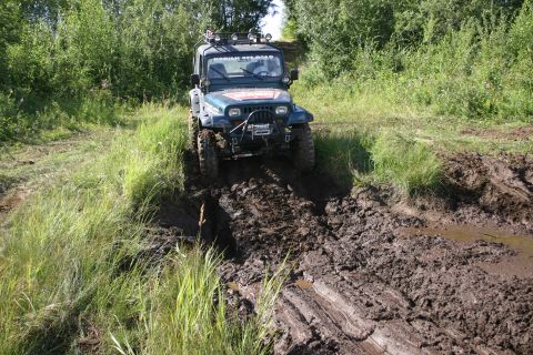 2003 Jeep TJ - A Jeep TJ navigates a challenging muddy trail surrounded by lush green foliage.