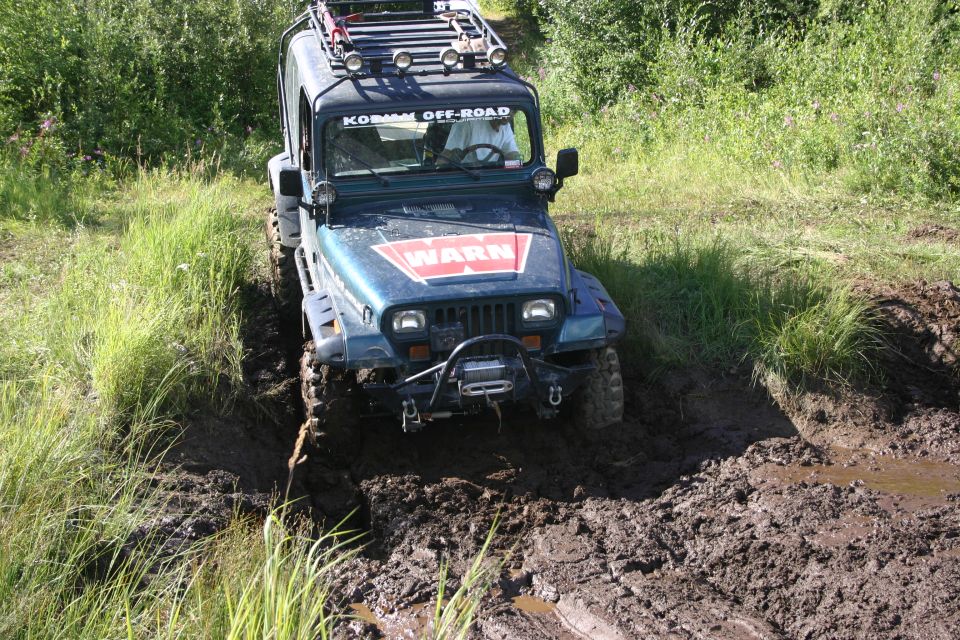 Dark green Jeep TJ with a roof rack and winch, stuck in mud, with a WARN decal on the hood