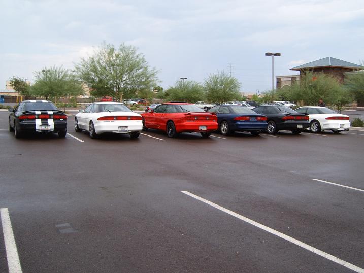 Row of five Ford Probe coupes parked rear-end-out in a lot, one black with white racing stripes