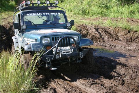 2003 Jeep TJ - A Jeep Wrangler navigates a challenging muddy terrain, kicking up dirt as it goes.