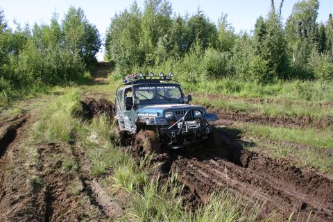2003 Jeep TJ - A blue Jeep Wrangler tackles a challenging muddy terrain, demonstrating its off-road capabilities.