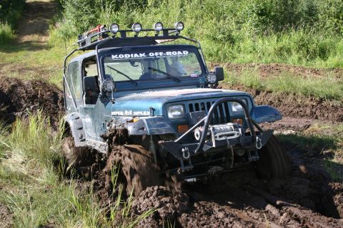 2003 Jeep TJ - Jeep Wrangler TJ navigates a muddy off-road trail, tires deep in the muck.