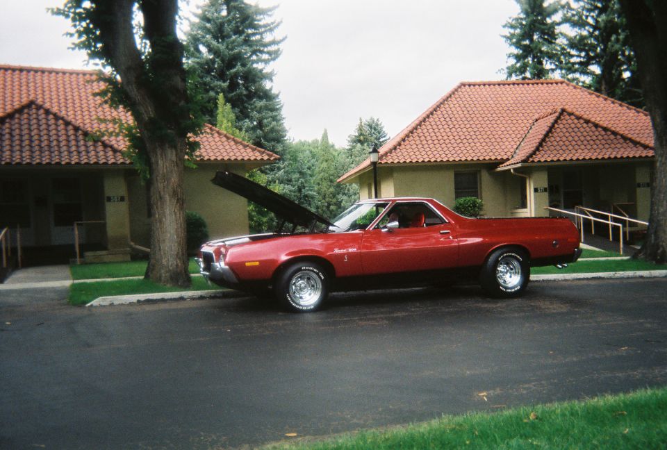 Red Ford Ranchero GT with hood open and chrome wheels, side view on a driveway