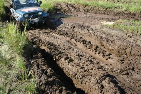 2003 Jeep TJ - A green Jeep Wrangler navigates a deep mud track, its front winch engaged.