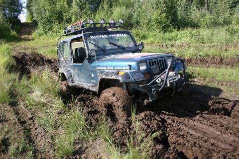 2003 Jeep TJ - A blue Jeep Wrangler navigates a muddy off-road trail, its tires deep in the muck.