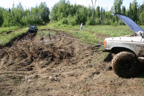 2003 Jeep TJ - Two SUVs are stuck in a muddy off-road track, with one vehicle attempting to tow the other.