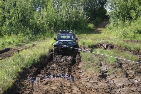 2003 Jeep TJ - A Jeep TJ navigates a challenging muddy terrain, with a winch line assisting its progress up a hill.