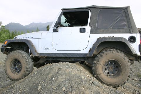 2003 Jeep TJ - A white Jeep Wrangler Rubicon is shown on a dirt mound with mountains in the background.