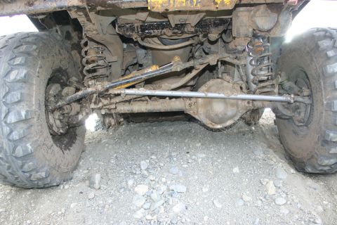 2003 Jeep TJ - The undercarriage of a heavily modified off-road vehicle is visible, with large tires and suspension components covered in mud.