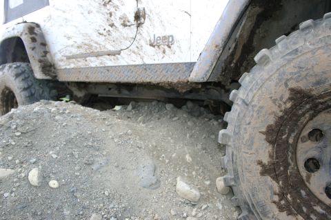 2003 Jeep TJ - A white Jeep TJ is shown from the side, covered in mud and resting on a pile of gravel.