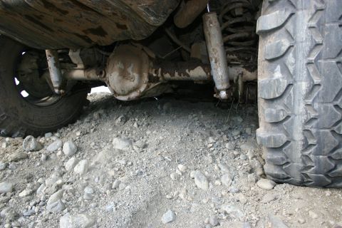 2003 Jeep TJ - Undercarriage view of a vehicle's rear axle and suspension system, showing the shock absorbers and coil springs on a rough, rocky surface.