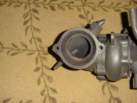 1995 Ford Mustang - A close-up view of a carburetor part, likely from an older vehicle, is shown against a patterned fabric surface.