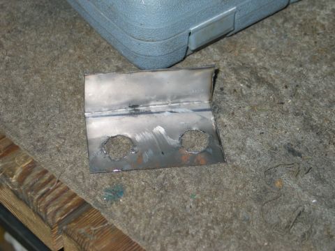 1995 Ford Bronco - A custom-fabricated metal bracket with two holes, likely for a vehicle project, rests on a textured surface.