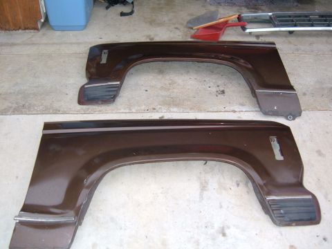 1985 Ford Bronco II - Two brown fender flares are laid out on a concrete floor next to a broom and dustpan.