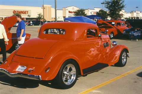1993 Ford Crown Victoria - A bright orange hot rod coupe with flame decals is parked at an outdoor car show.