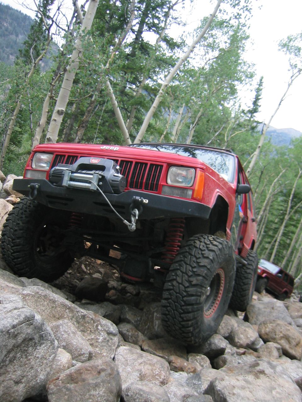 Red Jeep Cherokee with a winch on a rocky trail, another red Jeep in the background