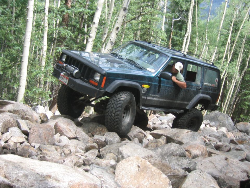 Dark green 1997 Jeep Cherokee off-roading over rocks, front 3/4 view