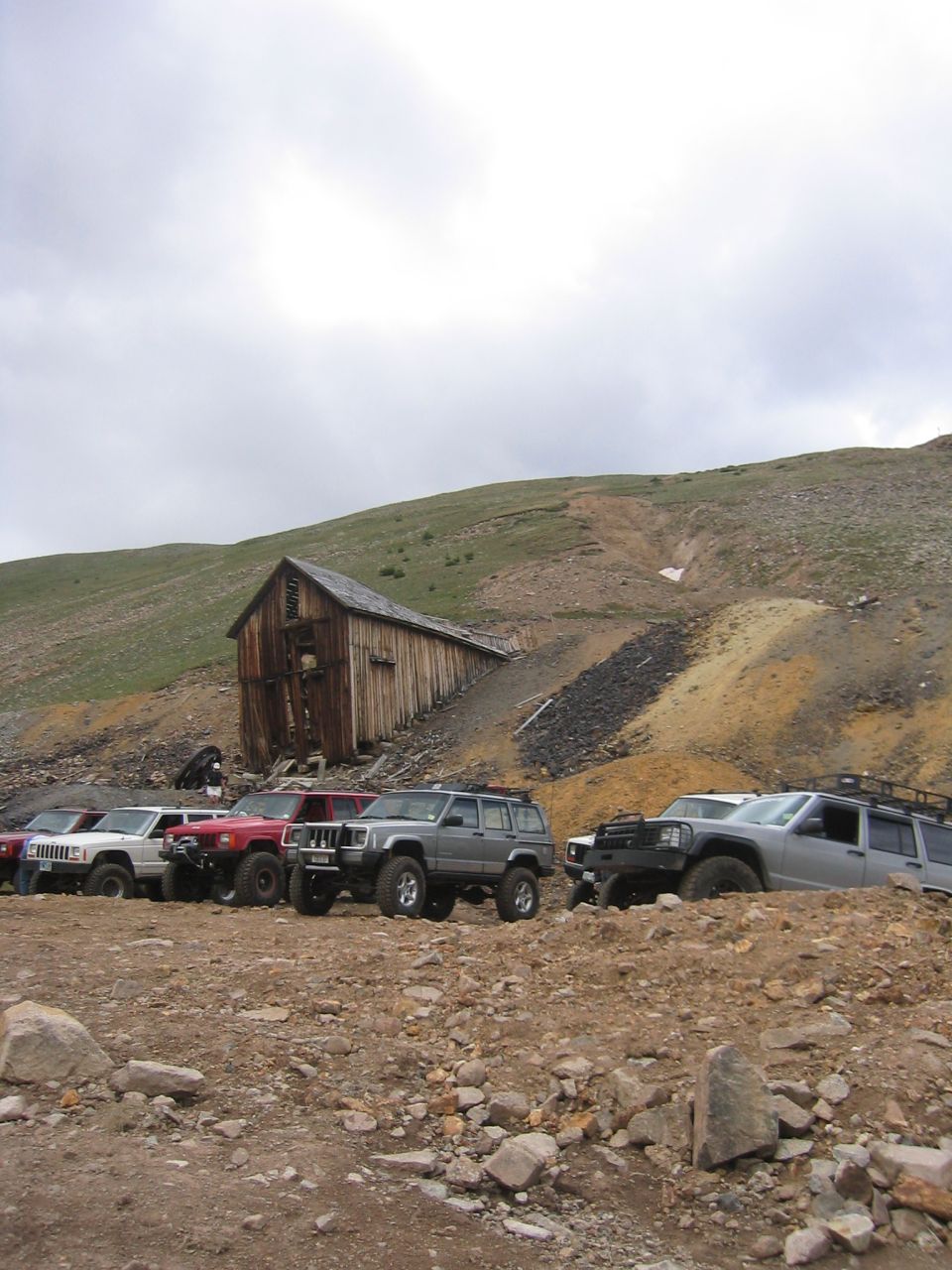 Several 1997 Jeep Cherokees parked on a rocky slope with an old wooden building behind them