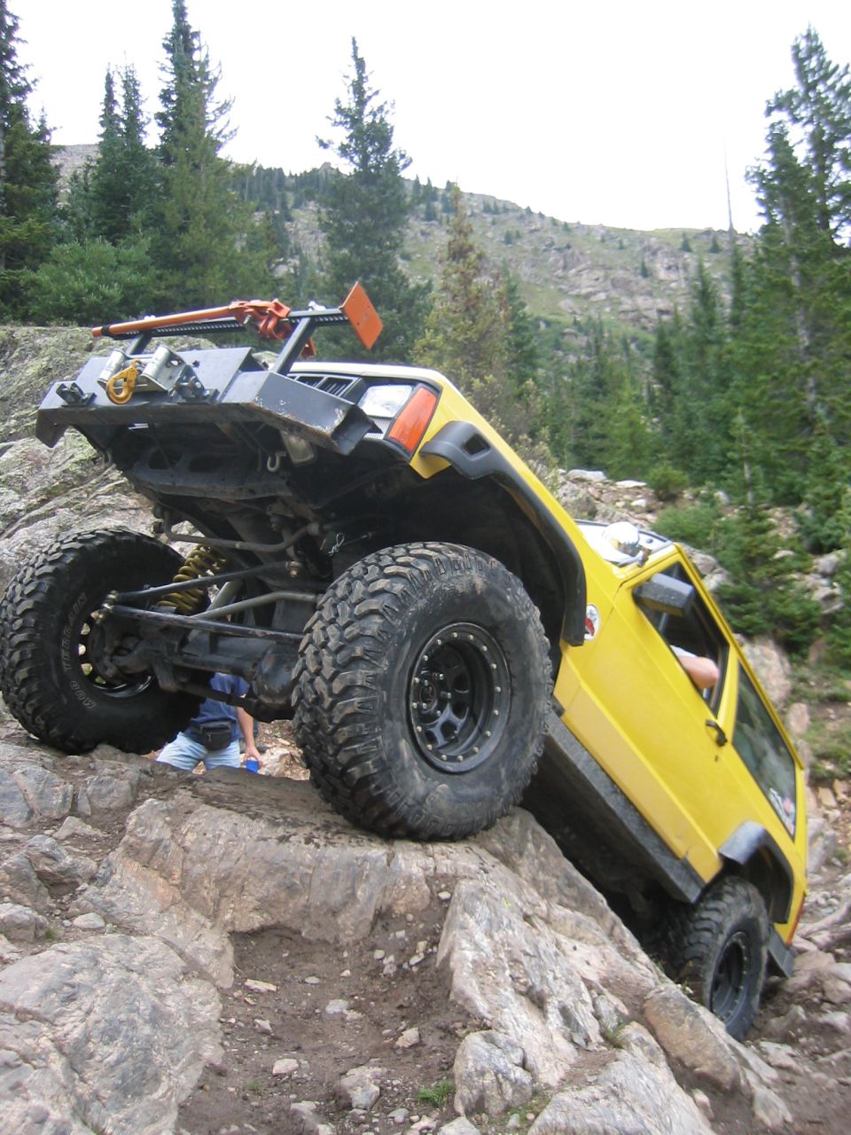 Yellow lifted Jeep Cherokee XJ climbing a granite rock face showing front axle, winch bumper and beadlocks