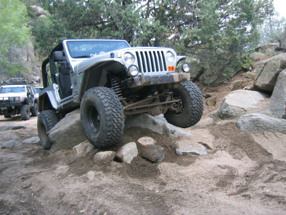 Silver Jeep Wrangler TJ crawling over rocks on a trail. Another white SUV is behind it