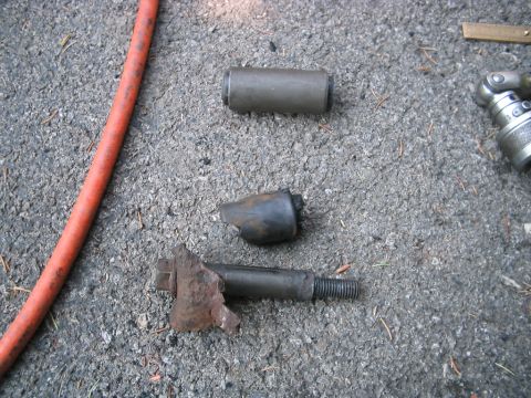 1992 Ford Bronco - Worn suspension parts, including a heavily corroded bolt and a broken bushing, lie on the ground next to a red hose and a socket wrench.