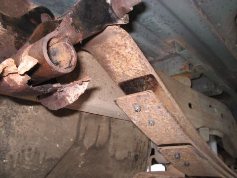 1992 Ford Bronco - The underside of a vehicle shows significant rust on the suspension components, including a leaf spring and bracket.