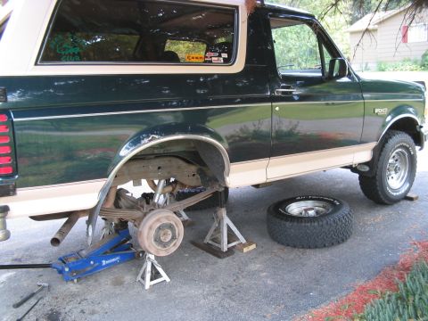 1992 Ford Bronco - A 1992 Ford Bronco is shown on jack stands with its rear wheel removed, indicating maintenance work is underway.