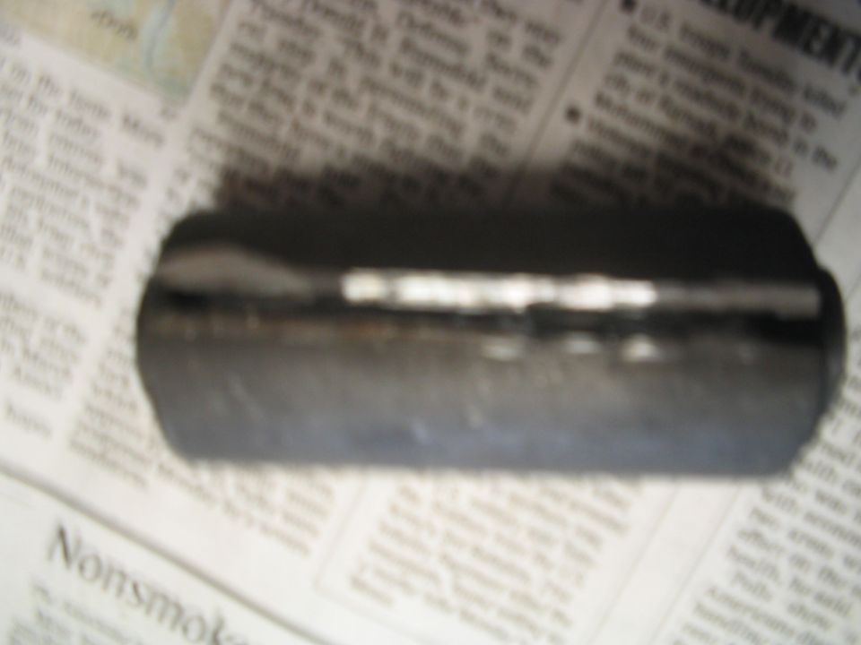Close-up of a dark, cylindrical automotive part resting on newspaper pages