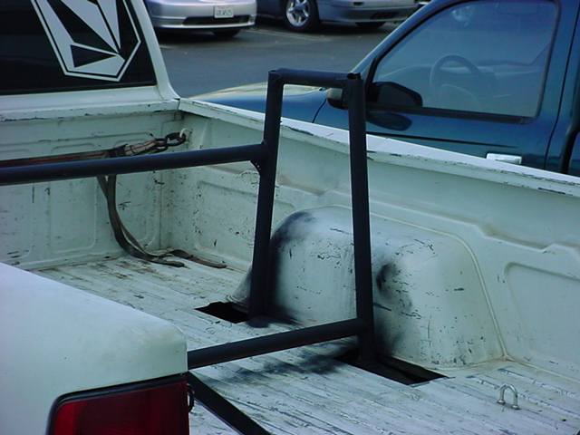 Pickup truck bed interior with roll bar, strap, and Volcom sticker on rear window. Other vehicles visible in background