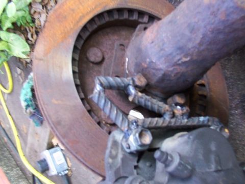 1993 Ford Bronco - A close-up view of a vehicle's brake system, a rusty rotor and caliper with a custom-made metal component.