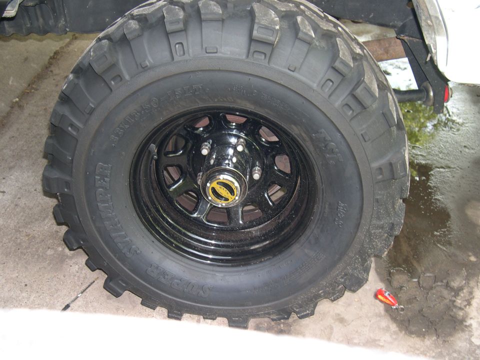 Oversized mud-terrain tire on a black steel wheel with chrome center cap, leaning on a vehicle
