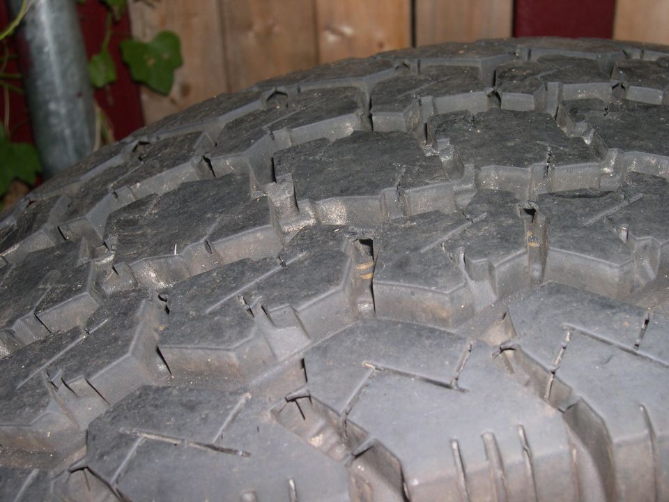 Close-up of dirty all-terrain tire tread with aggressive block pattern against a wood fence