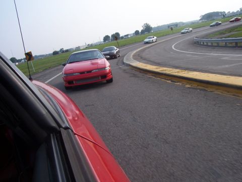 1990 Ford Probe - A red 1990 Ford Probe leads a pack of cars on a curving road.
