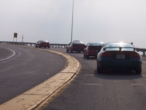 1990 Ford Probe - A line of coupes, including a dark green one with a spoiler, travels down a highway.